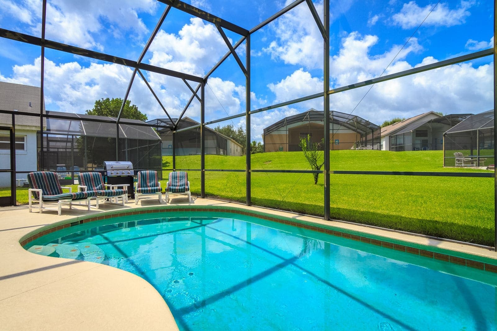 Mansard style aluminium screen enclosure over a pool and paver deck