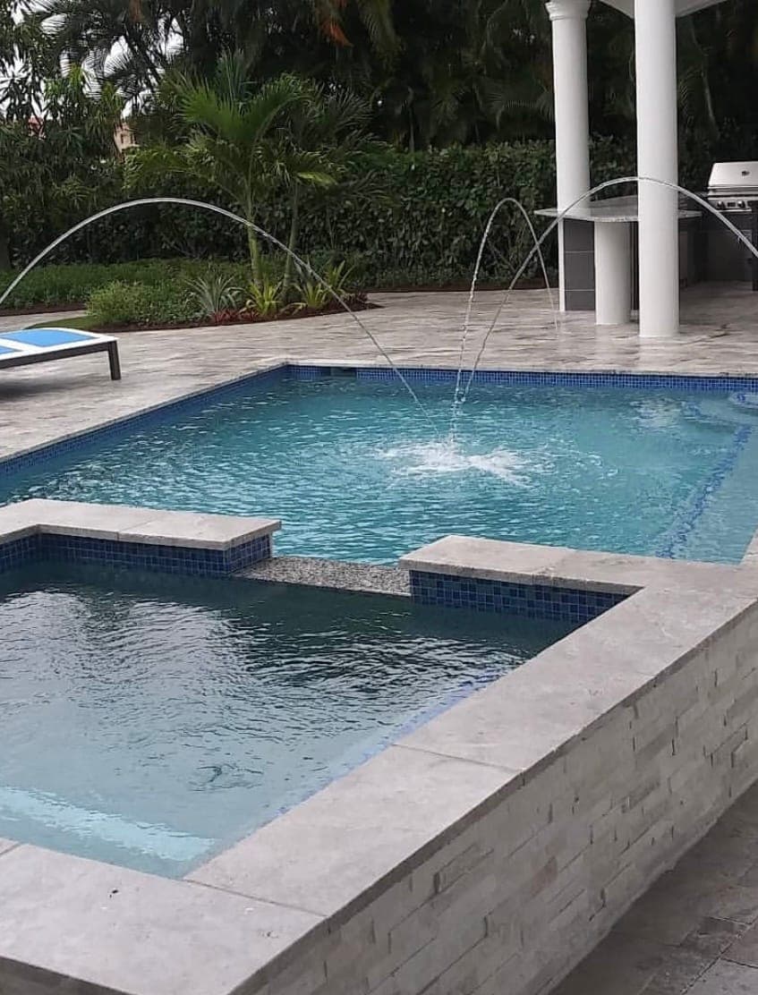 Rectangular pool with a raised spa, arcing deck jets, and a stone veneer bond beam