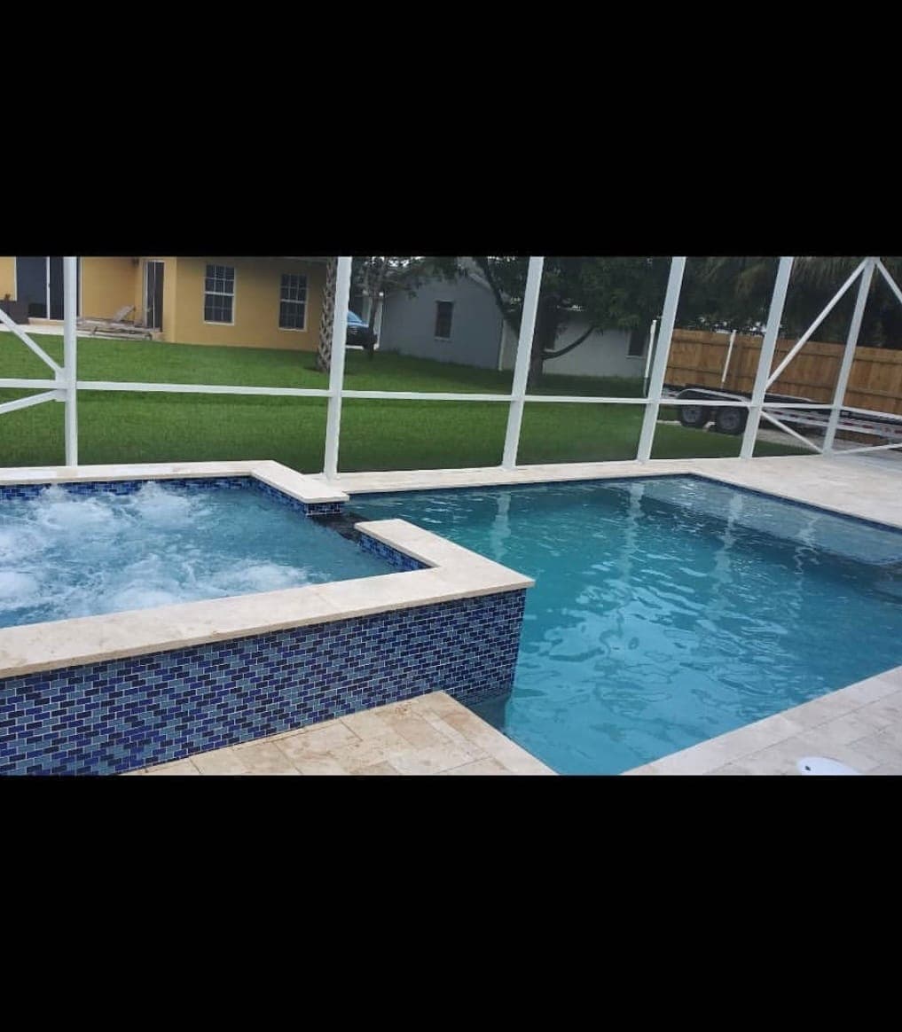 Pool and raised spa finished in blue glass tile, with a travertine deck under a white aluminum screen enclosure