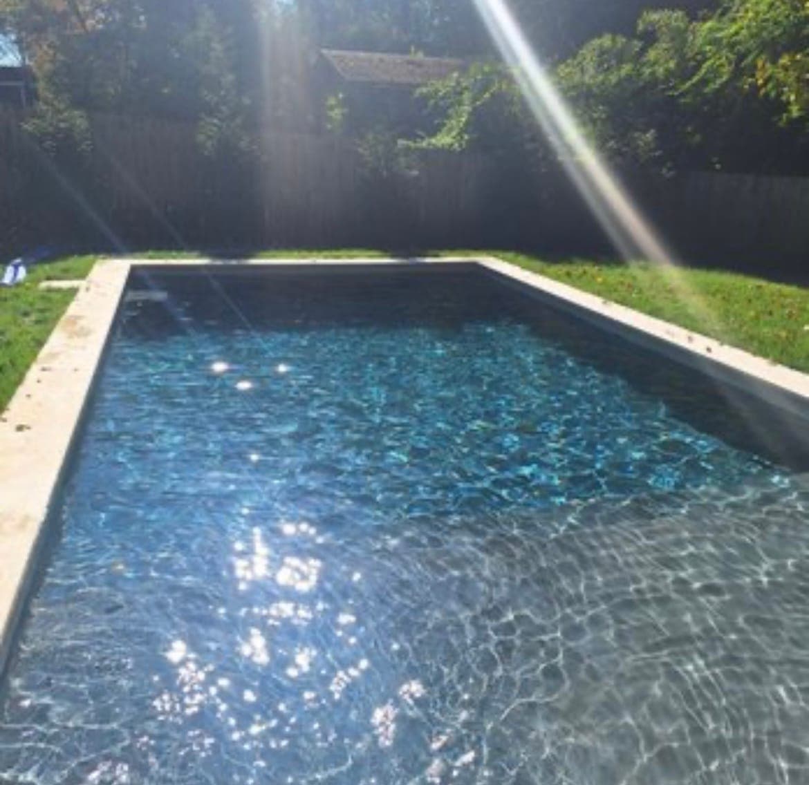 Rectangular pool with a dark interior finish and a narrow paver border set into a lawn