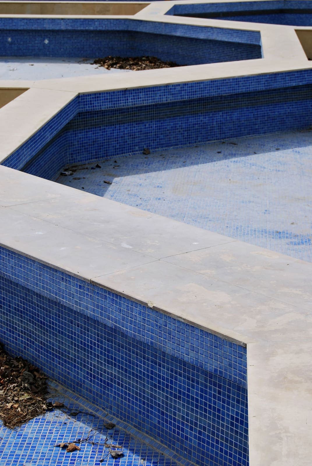 Blue waterline tile meeting light stone coping at the edge of a pool