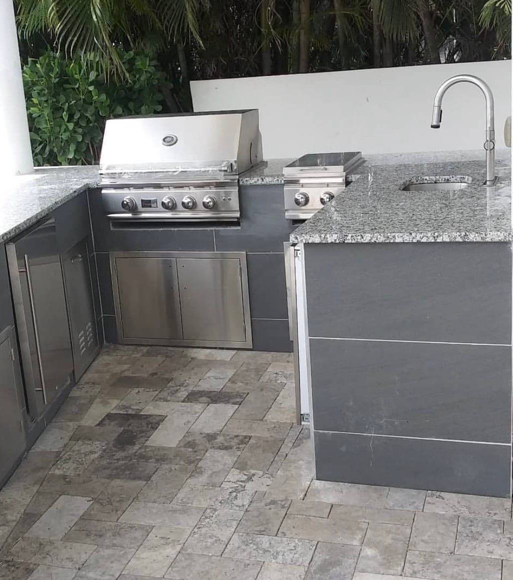 Stainless steel outdoor kitchen with a built-in grill and side burner, set on a travertine paver deck