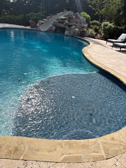 Freeform pool with curved travertine coping and a bubbling sun shelf