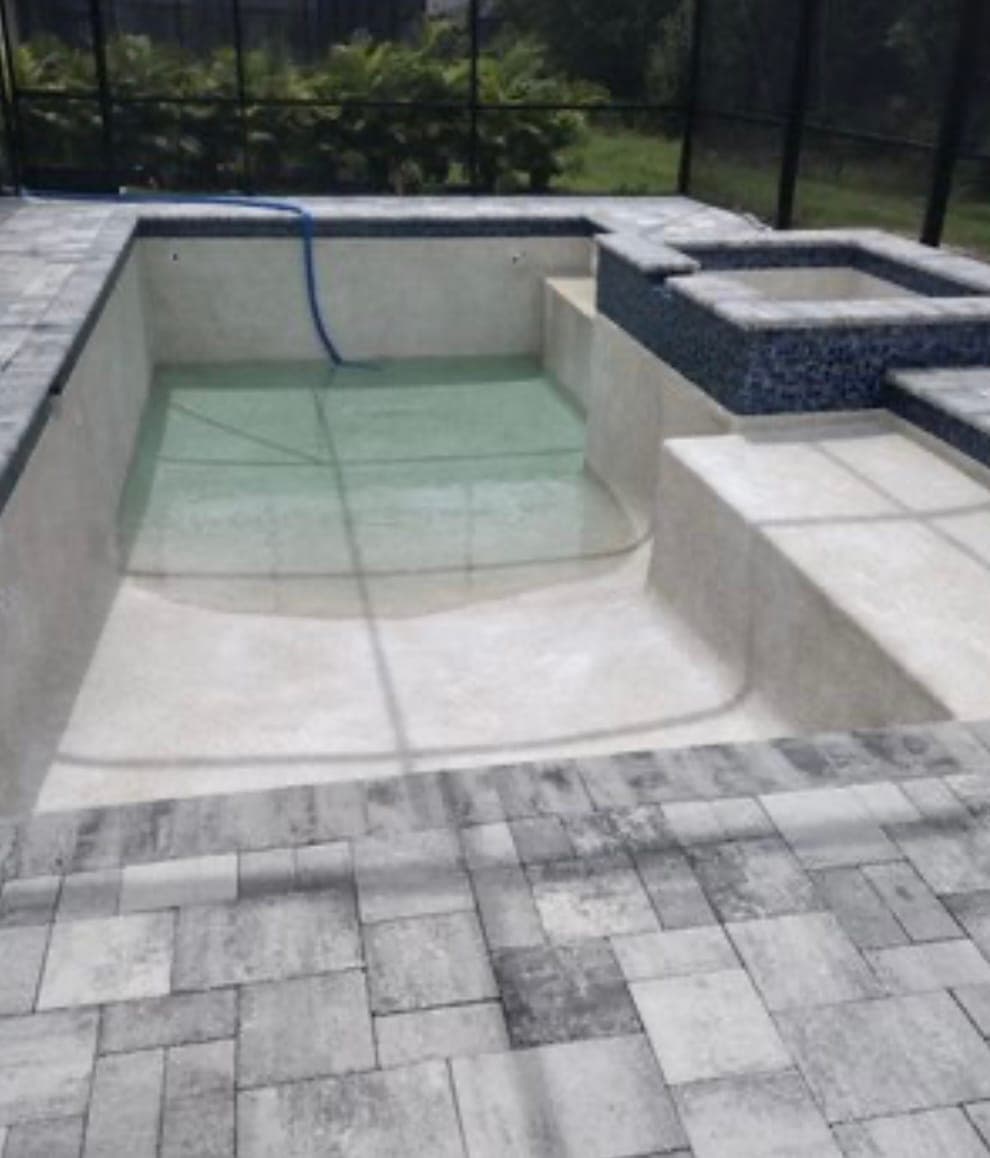 New pool shell with a raised spa in blue mosaic tile and a paver deck, inside a screen enclosure before the interior finish is applied