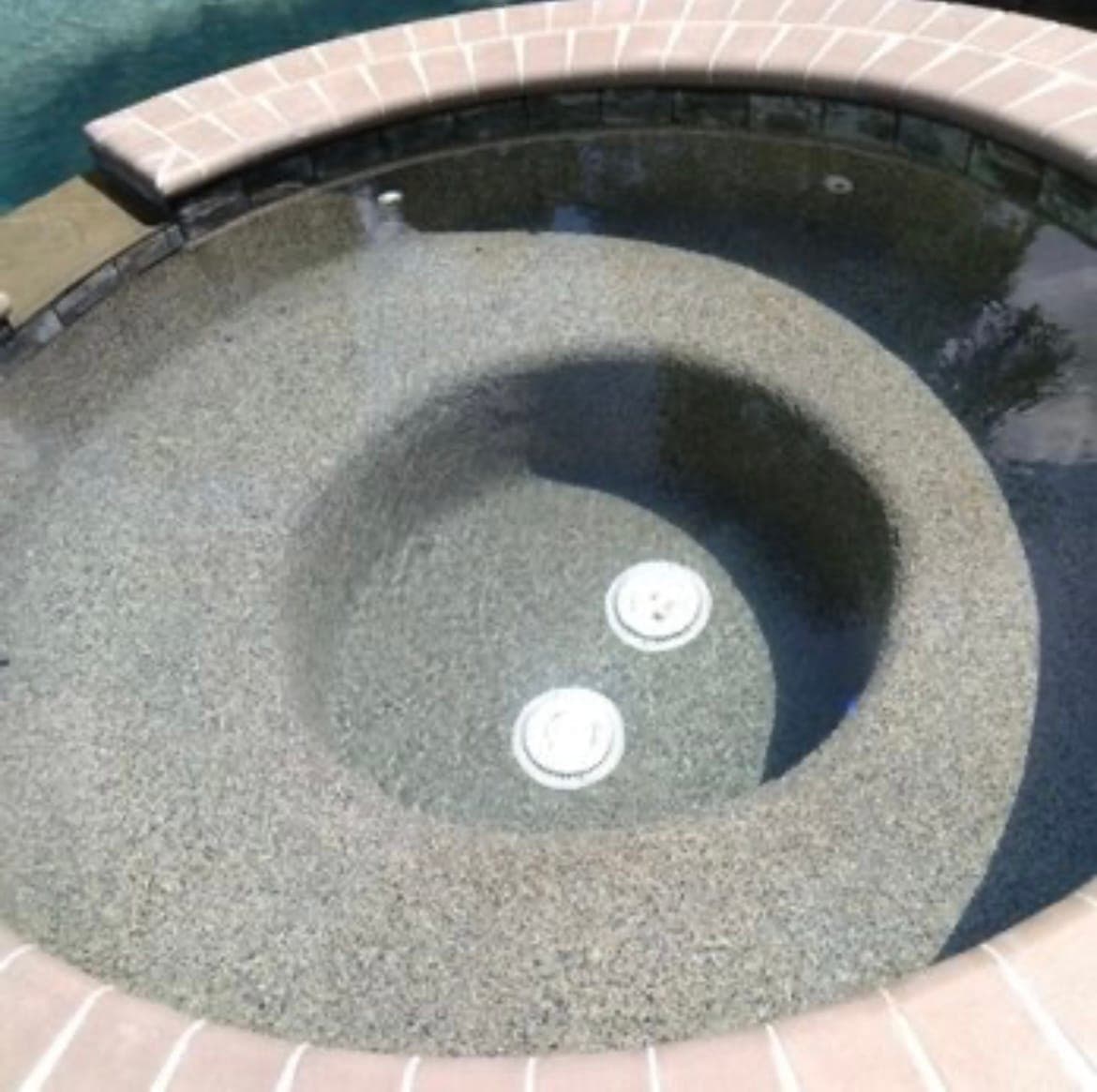 Round spa with a pebble interior finish, brick coping, and two therapy jets, spilling toward the pool